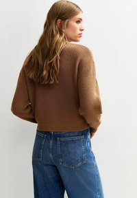 Brun, stickad kort tröja med en texturerad yta och lösa ärmar, tillsammans med högmidjade blå denimjeans.