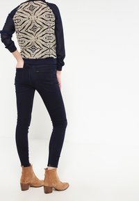 Marinblå tröja med beige blommönster broderat på ryggen, i kombination med mörk denimskinnyjeans och bruna ankelboots.