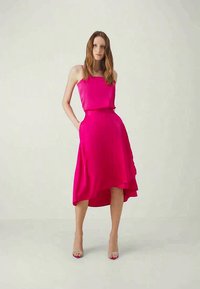 Fuchsia satin dress with a relaxed fit, featuring spaghetti straps, a cinched waist, and an asymmetrical hem that falls to mid-calf.