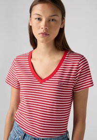 T-shirt à manches courtes rayé rouge et blanc avec un col en V, arborant un petit logo Levi's sur la poitrine gauche. En coton.