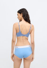 Sutien albastru deschis și pantaloni scurți asortați. Sutienul are bretele reglabile și închidere cu cârlig. Pantaloni scurți au o talie albă cu logo-ul "Calvin Klein".