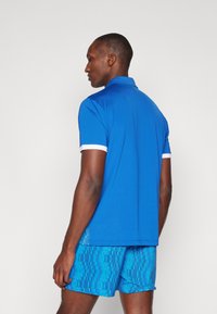 Men's blue polo shirt with a collar and white accents, paired with patterned blue shorts featuring vertical stripes and a relaxed fit.