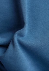 Tela de algodón azul con una textura suave, que presenta un delicado patrón acanalado y una caída suave, dispuesta en suaves pliegues.