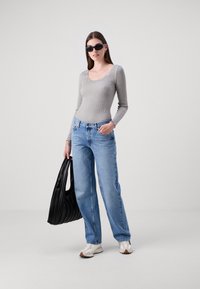 Gråstripet langermet topp med bølget hals, kombinert med lyseblå, løstsittende jeans, svart plissert tote bag og hvite joggesko.