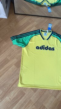 Tricou galben Adidas cu accente verzi, cu mâneci scurte și textură din plasă. Prezintă un logo mare în negru pe față și mâneci cu dungi.