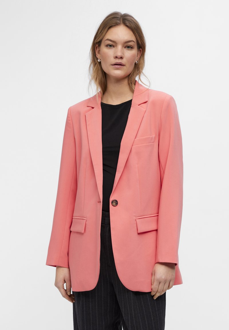 Coral pink blazer with two front pockets, single button closure, long sleeves, and notched lapels, paired with a black top and striped pants.