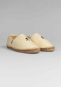 Espadrilles de lona en color beige con forma de puntera almendra. Presentan una suela de yute trenzado y detalles bordados en negro. Diseño ligero y casual.