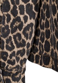 Tela con estampado de leopardo en una combinación de colores marrón y negro. Presenta una superficie texturizada y costuras visibles a lo largo del dobladillo.
