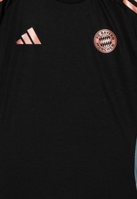 Crna kratka sportska majica s okruglim izrezom, s ružičasto zlatnim logom FC Bayerna München i tri horizontalne ružičasto zlatne pruge.