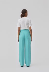 Pantalons à jambes larges en tissu turquoise éclatant, présentant une texture lisse et une taille ajustée. Associés à un t-shirt blanc uni.
