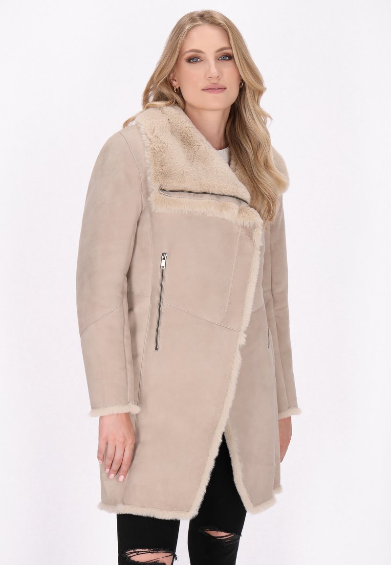 Cappotto in suede beige con colletto in pelliccia sintetica, tasca laterale con zip e bordo testurizzato. Design a lunghezza intermedia con un anteriore leggermente angolato.