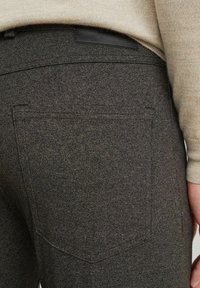 Tmavě šedé kalhoty s jemným vzorem, vybavené černou koženou nášivkou a klasickými zadními kapsami. Materiál působí odolně a strukturovaně.