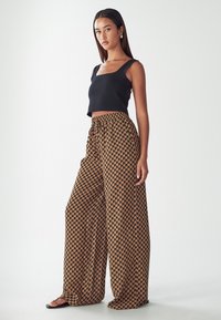 Black cropped tank top and wide-leg pants featuring a brown geometric pattern. Pants have an elastic waistband and a lightweight fabric.