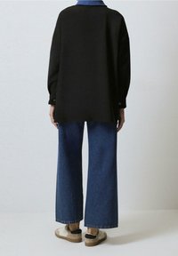 Chemise noire oversize avec un col bleu, associée à un jean bleu à jambes larges et des baskets beiges avec des accents foncés. Tissu doux et design décontracté.