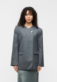 Γκρι προσαρμοσμένο σακάκι με δομημένους ώμους, ντεκολτέ σε σχήμα V και δύο μπροστινές τσέπες. Διαθέτει ασημένιο καρφίτσα διακόσμηση στο πέτο.