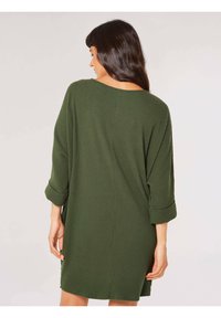 Olivgrünes, geripptes Strickkleid mit lockerer Passform, Fledermausärmeln und weitem Ausschnitt. Seitliche Schlitze verbessern den Komfort und die Bewegungsfreiheit.