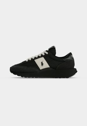 Baskets noires avec des lacets blancs et un patch latéral blanc présentant un logo cheval et cavalier, montrées de profil sur un fond uni.