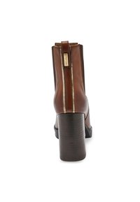 Botín de cuero marrón hasta el tobillo con un alto tacón cuadrado, que presenta un detalle de cremallera metálica dorada y una textura suave. La vista posterior resalta el diseño.