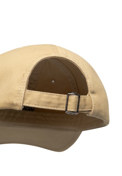 Beigen värinen baseball-lippalakki, jossa säädettävä kangasremmi metallisoljella takana valkoista taustaa vasten.