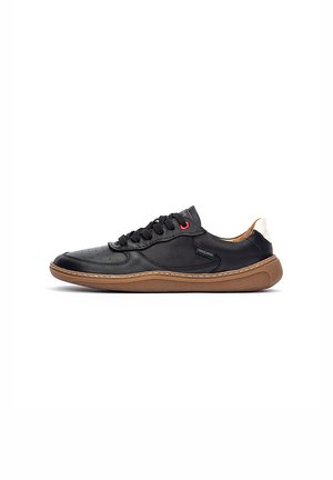 Zapatilla de cuero negra con suela de goma, punta redondeada, talón beige en contraste y acento rojo en los cordones. Detalles texturizados en los laterales.