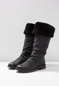 Bottes noires en cuir jusqu'au genou avec un large revers en fausse fourrure noire, bout arrondi et semelle texturée basse. Surface lisse avec un léger design affaissé.
