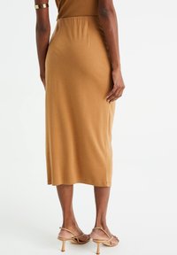 Hnědá midi sukně z měkké látky s elegantním střihem a jemným pasovým lemem. Kombinováno s nahými páskovými podpatky.