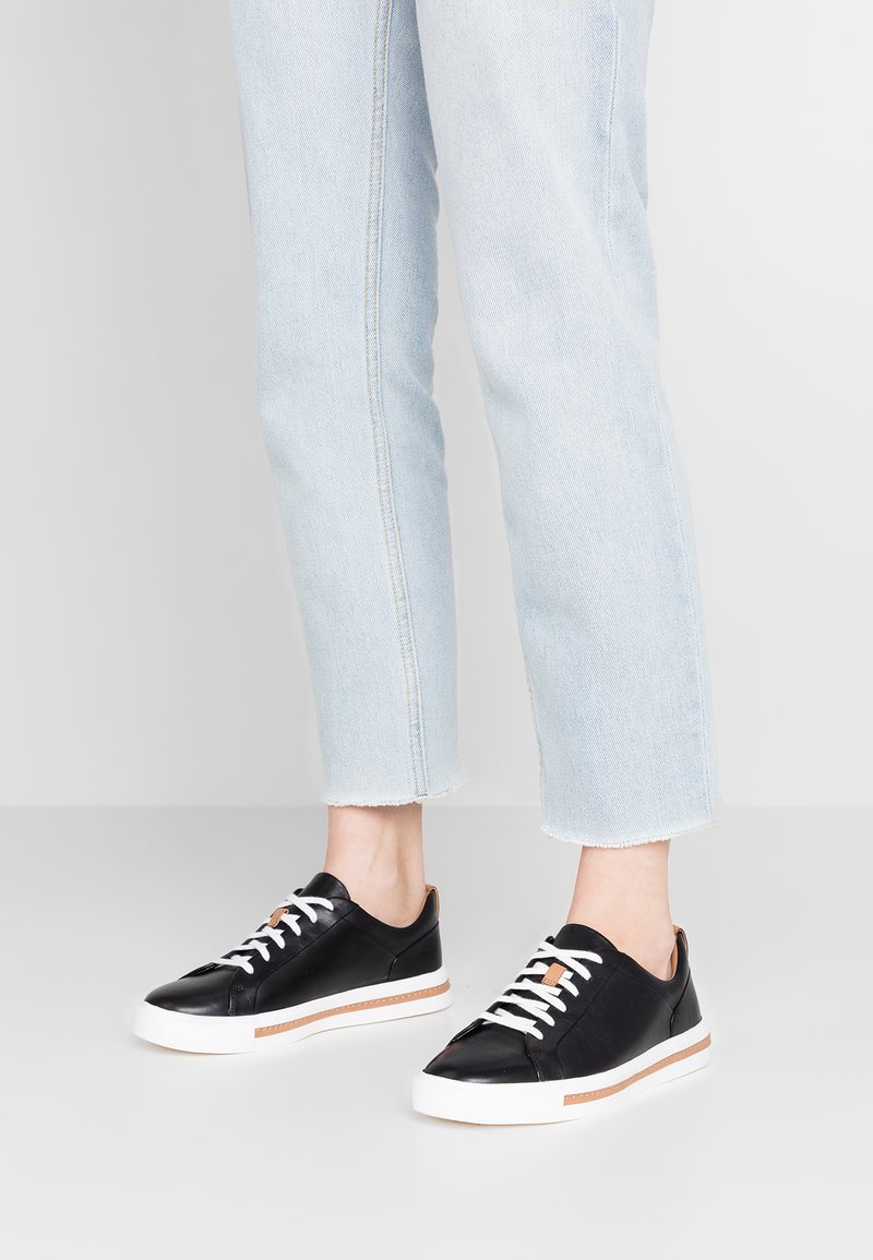 Baskets en cuir noir avec des lacets blancs, des accents contrastants en tan et une semelle texturée. Associées à un jean en denim bleu clair, cropped.