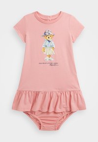 Vaaleanpunainen puuvillamekko, jossa on röyhelöinen helma. Mekossa on karhukuva, jossa karhu on pukeutunut siniseen paitaan ja hattuunsa. Lyhyet hihat, pehmeä materiaali ja joustava helma.