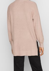 Maglione lavorato a maglia rosa chiaro con una vestibilità rilassata, texture a coste e spacchi laterali, dotato di maniche lunghe e un design orlo asimmetrico.