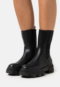 Sorte skinnankleboots med elastiske sidepaneler, en chunky plattformsåle og en glatt, matt overflate. Lettere med en teksturert såle.