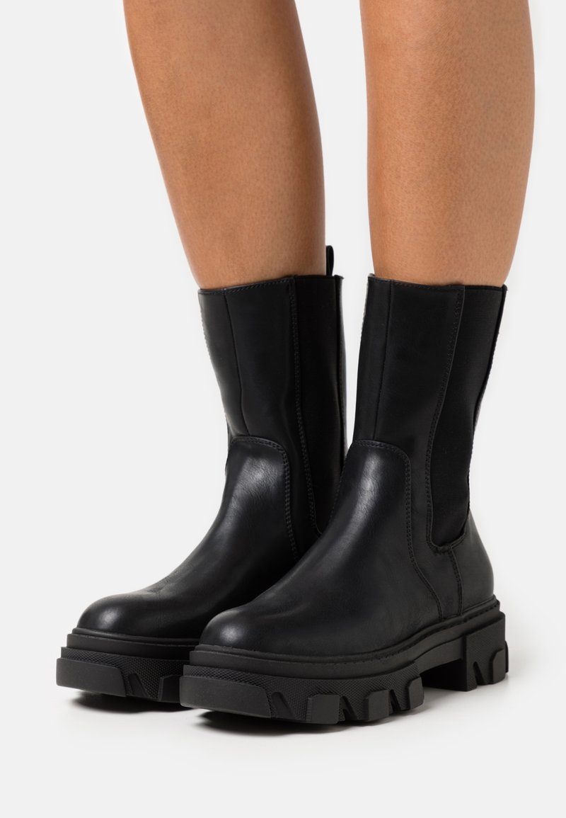 Sorte skinnankleboots med elastiske sidepaneler, en chunky plattformsåle og en glatt, matt overflate. Lettere med en teksturert såle.