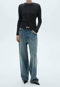 Cardigan gris foncé côtelé à manches longues, boutonné sur le devant, associé à un jean bleu clair à coupe décontractée et des escarpins noirs pointus.