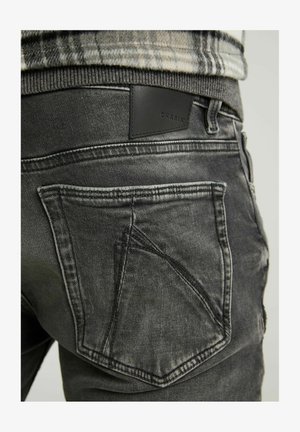 Jeans in denim grigio scuro con una texture leggermente usurata. Presentano un design con tasca posteriore angolare e una patch del marchio in pelle nera in vita.