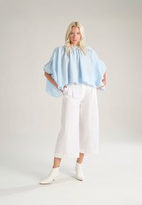 Top corto azzurro chiaro con texture, scollatura rotonda e bottoni, abbinato a pantaloni bianchi a gamba larga e stivaletti bianchi a punta.