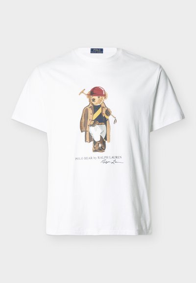 Λευκό μπλουζάκι με γραφικό μιας αρκούδας που φοράει κόκκινο κράνος, καφέ παλτό, ριγέ πουκάμισο, λευκό παντελόνι, κρατώντας ματσόλα πόλο, και κείμενο από κάτω.