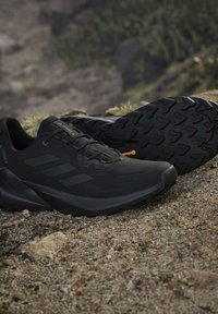 Zwarte Adidas Terrex trail running schoenen rustend op rotsachtige ondergrond met zichtbare robuuste zool en buitenachtergrond.