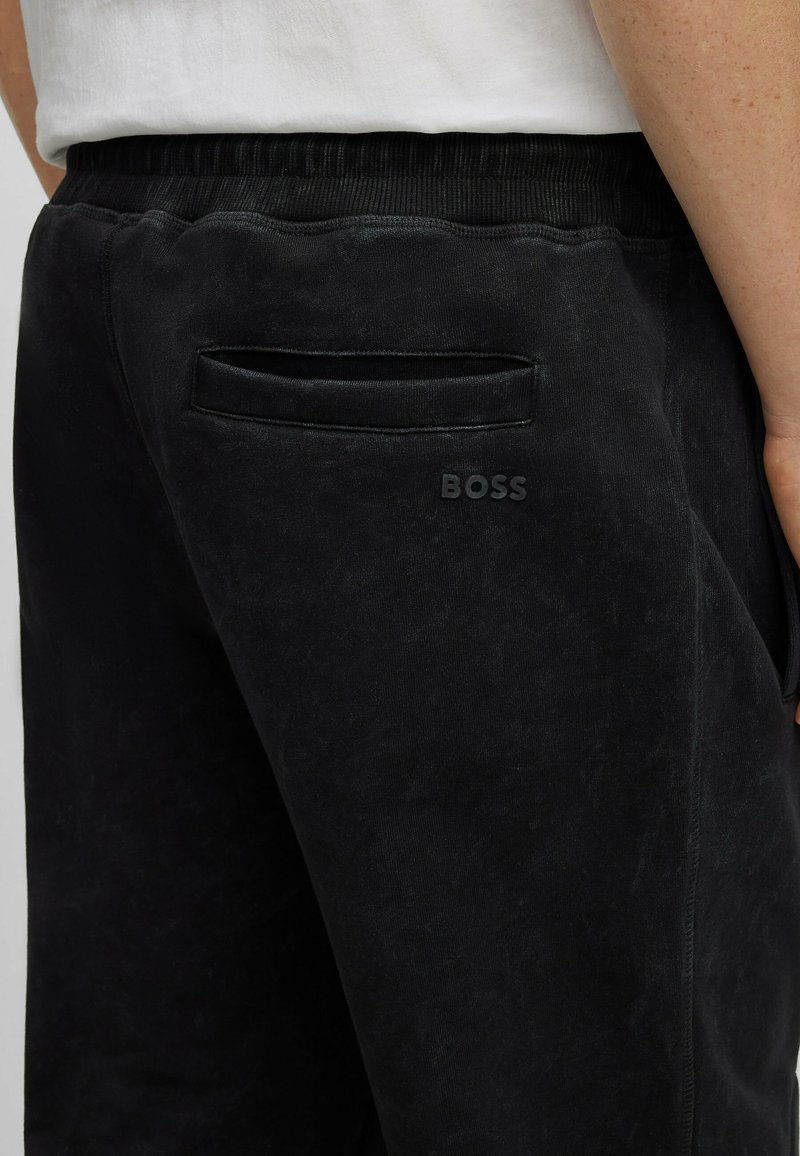 Pantaloni della tuta neri con una texture liscia, vita elasticizzata, tasca posteriore e logo "BOSS" in rilievo sulla parte inferiore.