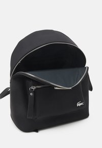 Sac à dos noir avec extérieur texturé, grande ouverture zippée et doublure noire unie. Comprend une poche frontale et des accents métalliques argentés.