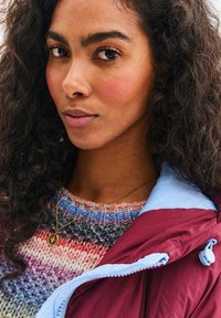 Mnohobarevný pletený svetr s gradientním vzorem v modré a růžové barvě, doplněný o vínový a světle modrý zipový kabát s šňůrkou.