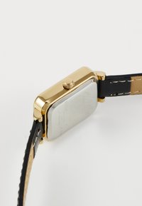Reloj rectangular dorado con una caja de metal pulido, correa de cuero negro y una esfera de reloj texturizada de color claro. Incluye una corona lateral.