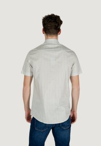 Camicia a maniche corte in tessuto leggero con motivo geometrico in colori tenui. Dotata di colletto classico e orlo curvo; abbinata a jeans blu.