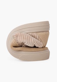 Zapato beige sin cordones con un upper de tela texturizada y una suela de goma moldeada. El diseño plegado presenta suaves acentos de ante y detalles acanalados.