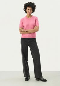 Un pull léger rose à manches courtes avec un col rond, associé à un jean large noir taille haute et des chaussures à plateforme noires.