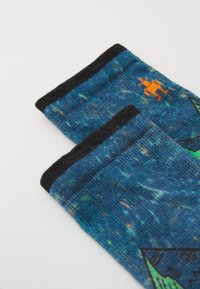 Calcetines azules con un estampado y un puño negro que presenta un pequeño gráfico de un canguro naranja. Hechos de una tela suave y texturizada con un diseño colorido.