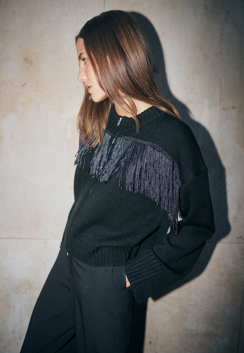 Schwarzer Strick-Cardigan mit strukturiertem Design und Fransen-Detail in Grautönen, mit entspannter Passform und Reißverschluss.