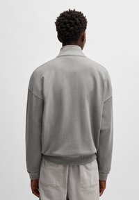 Grå hettegenser med høy krage og ribbede mansjetter og kant. Myk stoff, avslappet passform, med innsydde ermer. Minimalistisk design.