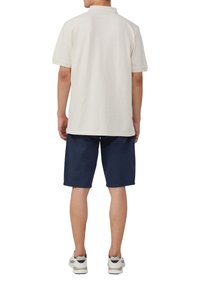 Polo à manches courtes en tissu écru, associé à un short bleu marine, vu de dos, avec un col classique et une coupe décontractée.