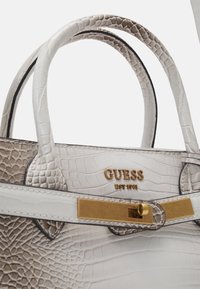 Hvid håndtaske med krokodilleskindspræg, gulddetaljer og teksturerede stropper. Har en logoplaket og et struktureret design.