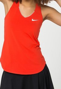 Rode Nike mouwloze sporttop met een V-hals, gemaakt van een soepele, lichte stof. Witte Nike-logo op de linkerborst.