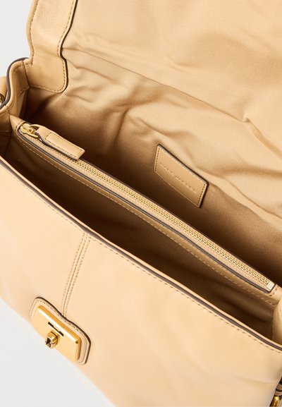 Μπεζ δερμάτινη τσάντα χειρός ανοιχτή για να εμφανιστεί η λείο ύφασμα εσωτερική επένδυση και μια εσωτερική τσέπη με φερμουάρ, με χρυσό φερμουάρ και κλείσιμο με χρυσή αγκράφα.